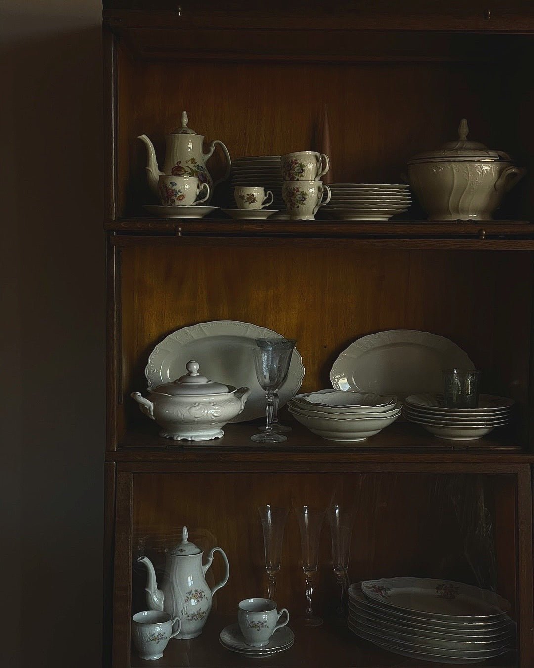 Fine art photography print of a vintage wooden cabinet displaying antique porcelain teapots, china and crystal in warm nostalgic tones, by Israeli artist Tamar Green