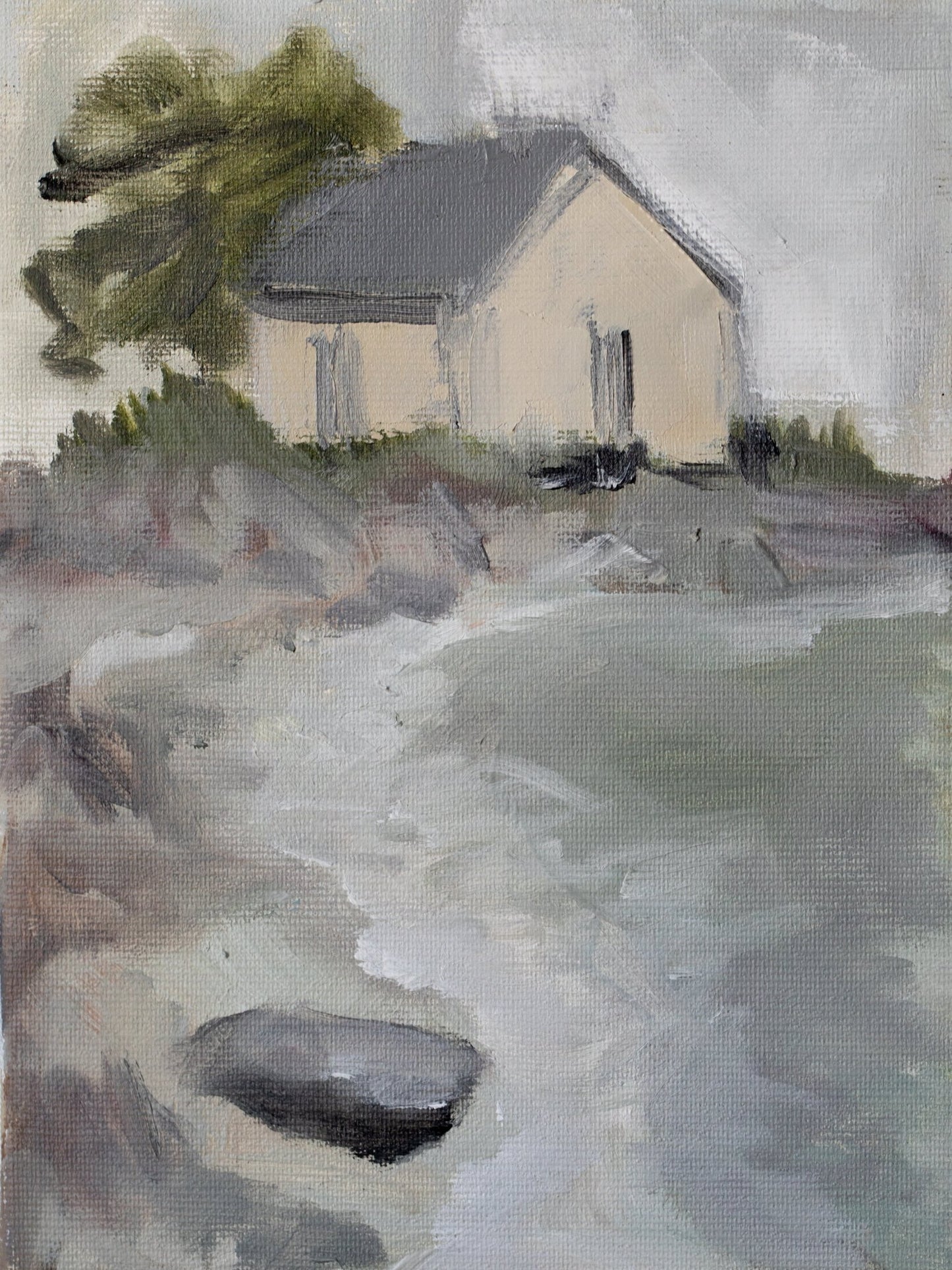 Original oil painting of a cream-walled house with grey roof at the edge of water with rocks and a leaning tree, from the Home series by Israeli artist Tamar Green